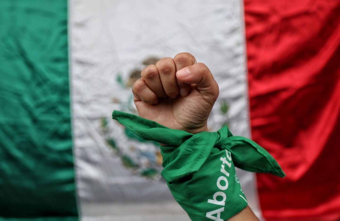 En la imagen una mujer posa con pañuelo verde símbolo del aborto legal, frente a una bandera de México durante el dictamen de la SCJN