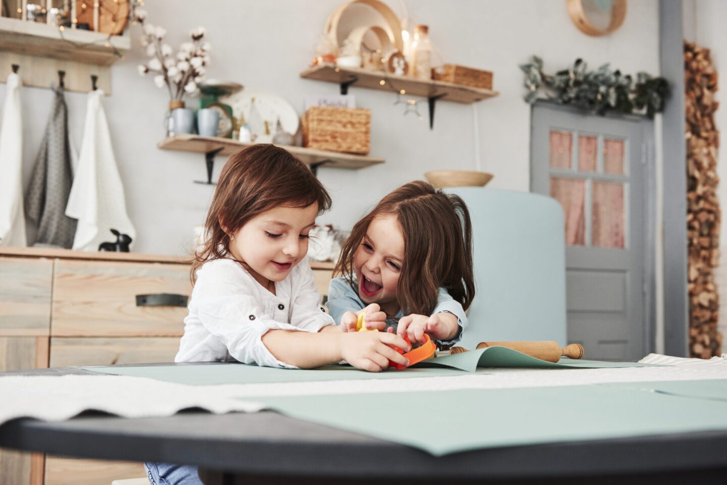 Happy childhood. Two kids playing with yellow and orange toys in the white kitchen