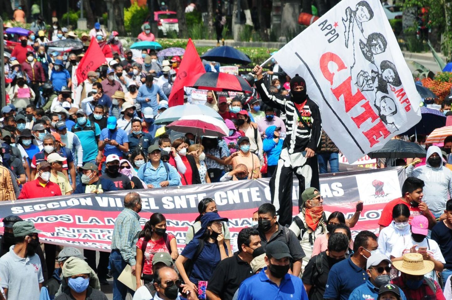 Un hombre en zancos agita una bandera en medio de la marcha de la CNTE.