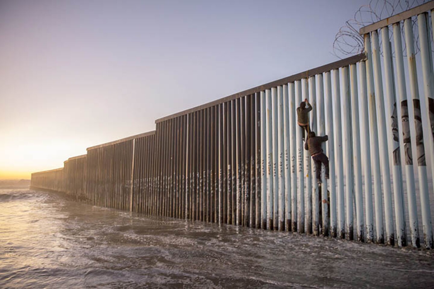 Pareja de migrantes centroamericanos saltan el muro fronterizo en Tijuana