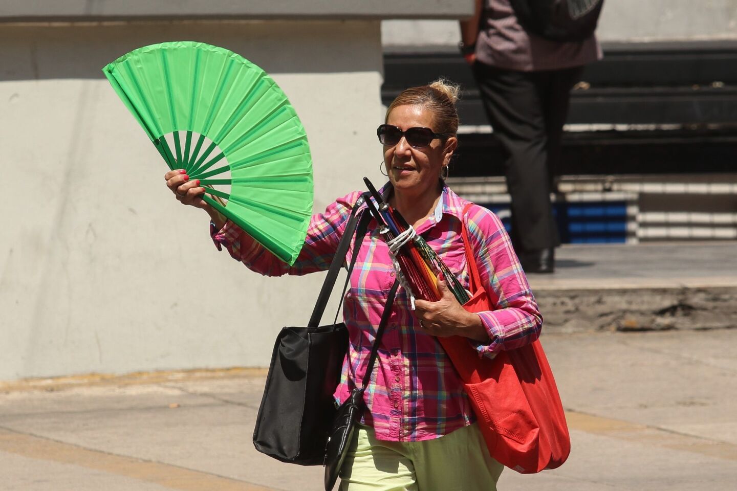 Debido al intenso calor en la ciudad una mujer se refresca con un abanico mientras camina por Paseo de la Reforma.