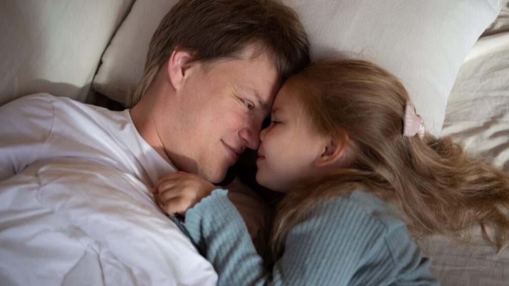 little cute girl hugging her dad while lying in bed