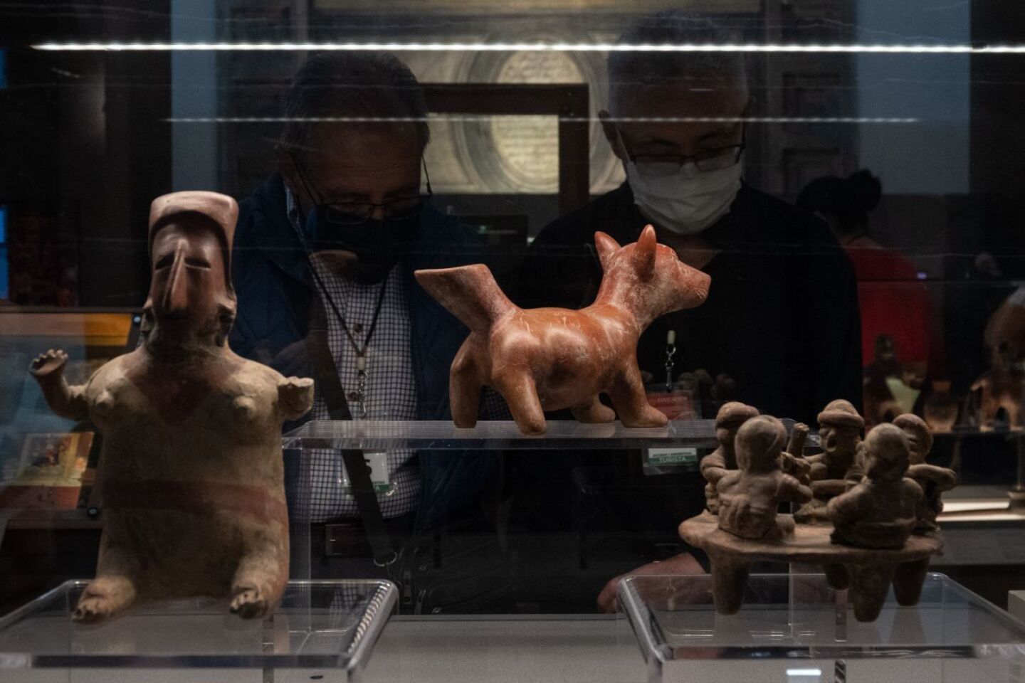 Dos hombres observan piezas prehispánicas de arcilla y barro exhibidas en la exposición "La Grandeza de México" en el salón Iberoamericano de la SEP.