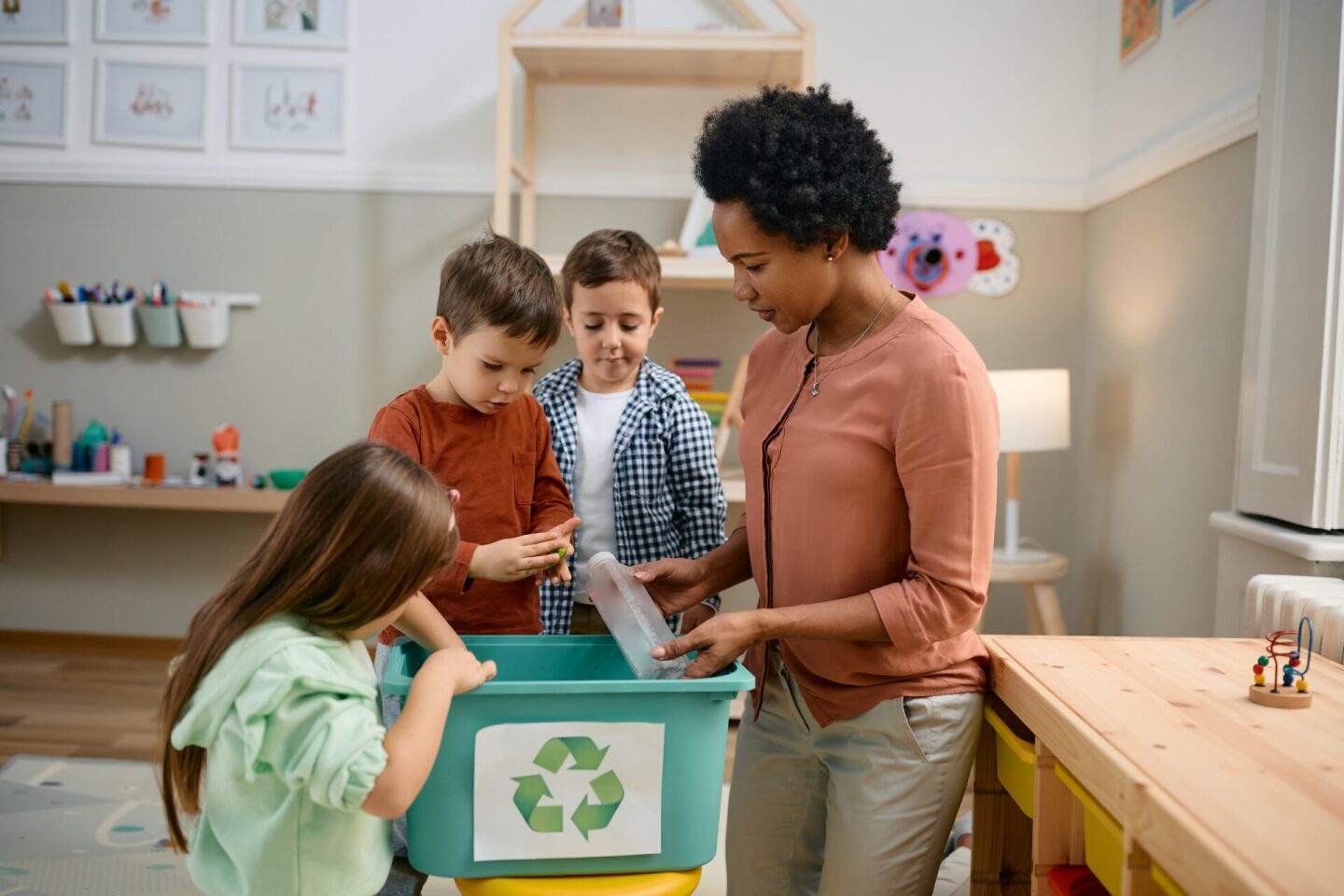 Small kids learning to recycle with help of their African American teacher at preschool.