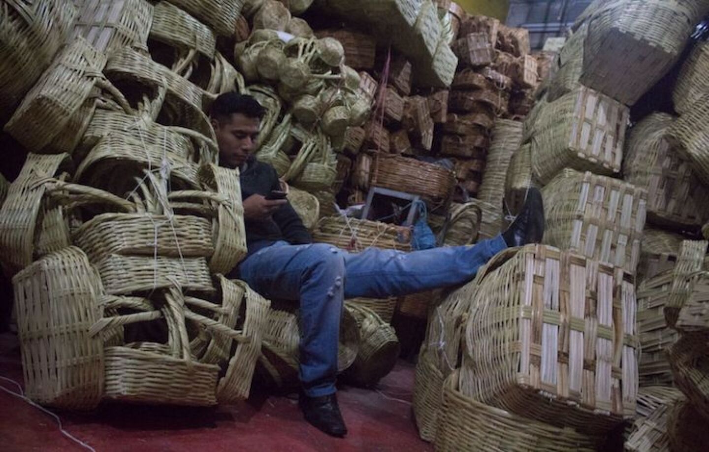 Un artesano del mercado de la Merced descansa sentado entre canastas de carrizo.