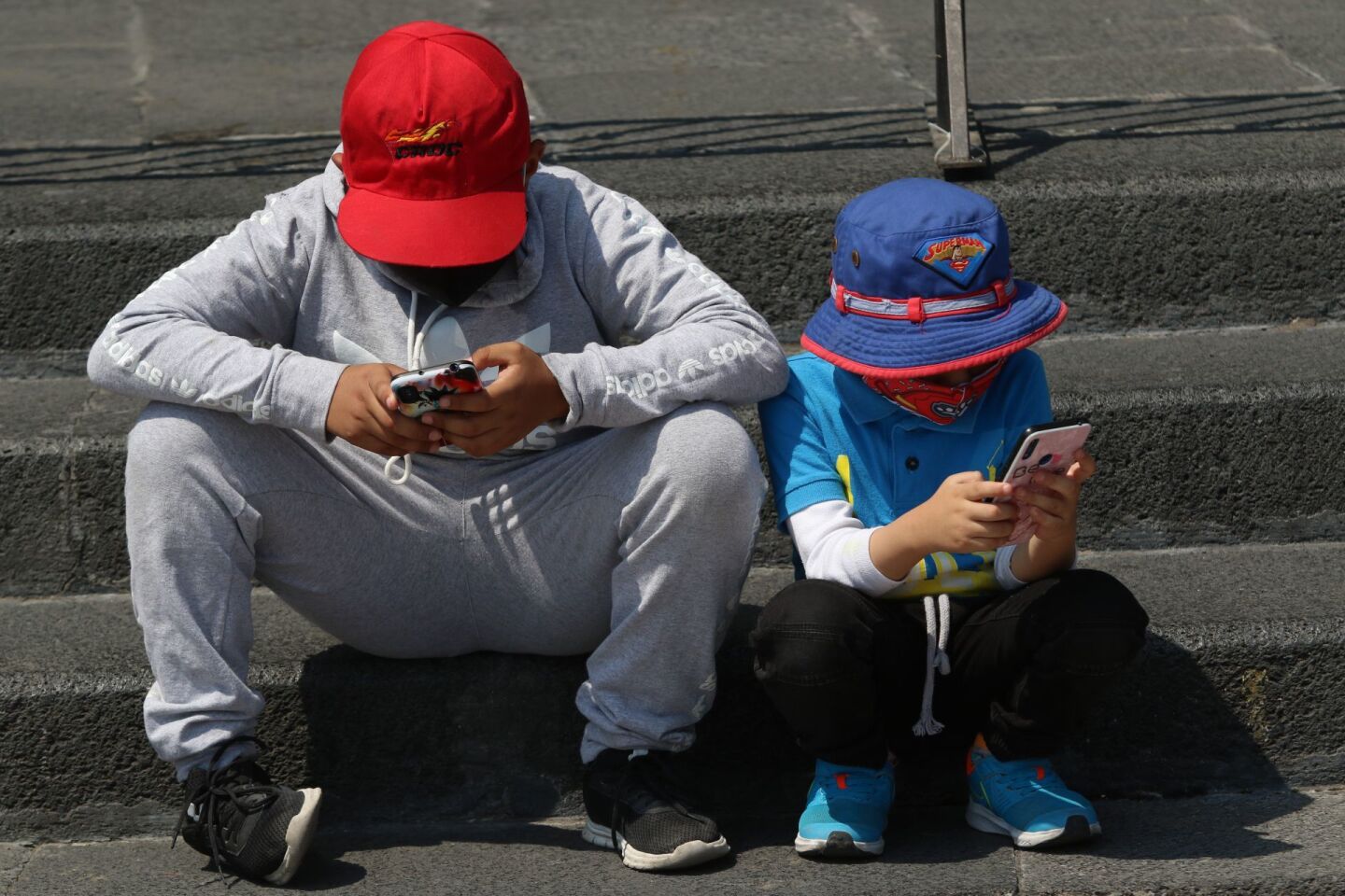 Un par de niños se entretienen con sus respectivos celulares.