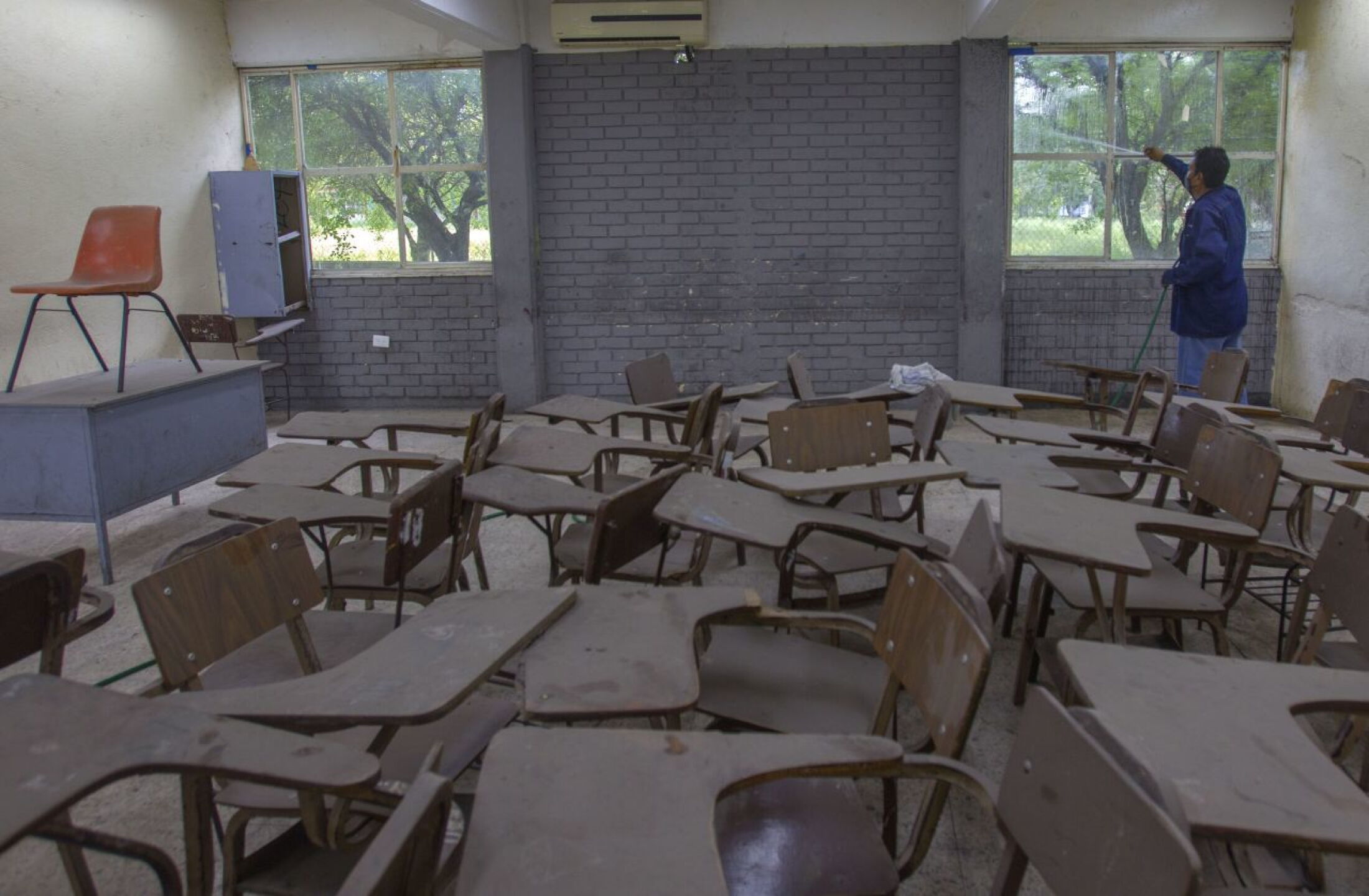 Personal educativo realiza labores de limpieza en un aula de una escuela secundaria ante un posible regreso a clases presenciales.