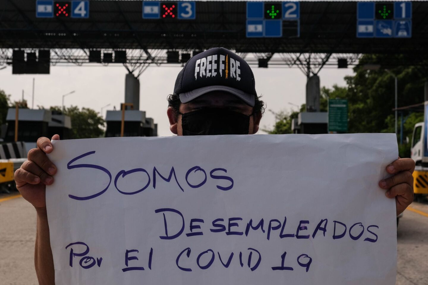 Un mesero desempleado muestra una pancarta a los conductores que pasan por la Caseta de Cobro de la carretera Tuxtla - San Cristóbal de las Casas, solicitando su apoyo.