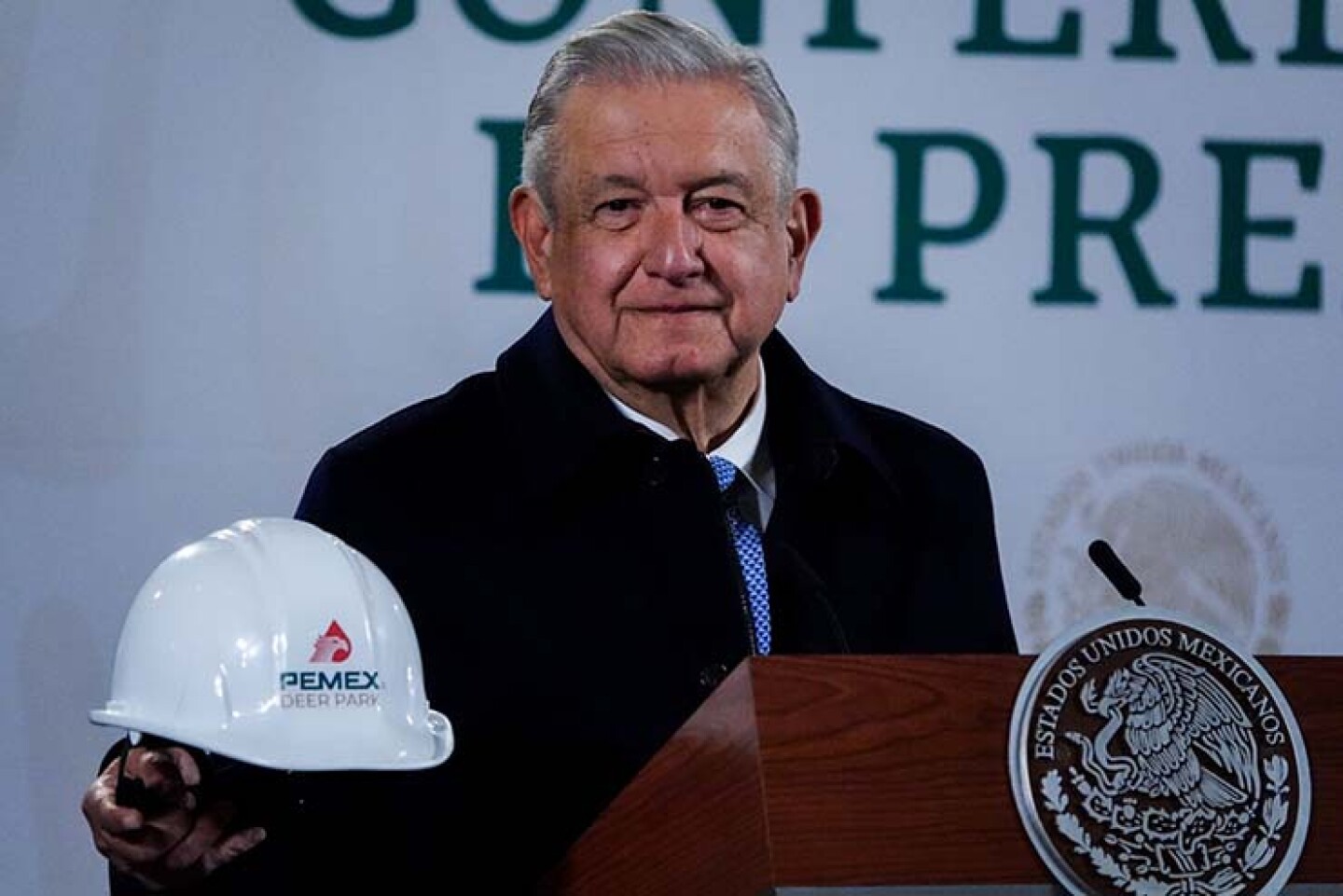Andrés Manuel López Obrador sostiene un casco con lo que será el nuevo logo de la refinería Deer Park durante la conferencia matutina.